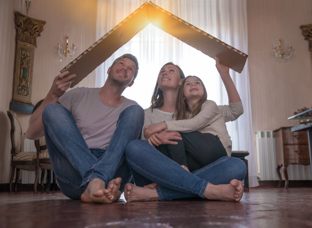 Kleine Familie die mit einem Karton ein Hausdach formt.